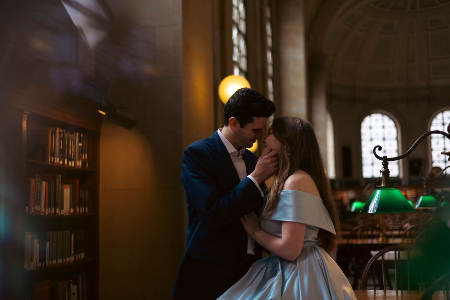 Two people share an intimate moment while dancing in a dimly lit library with stained glass windows in the background.