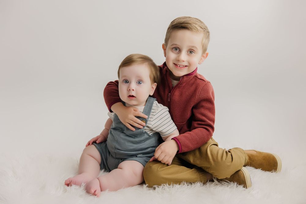 Cheerful siblings lounging together on a cream colored backdrop in coordinating casual outfits.