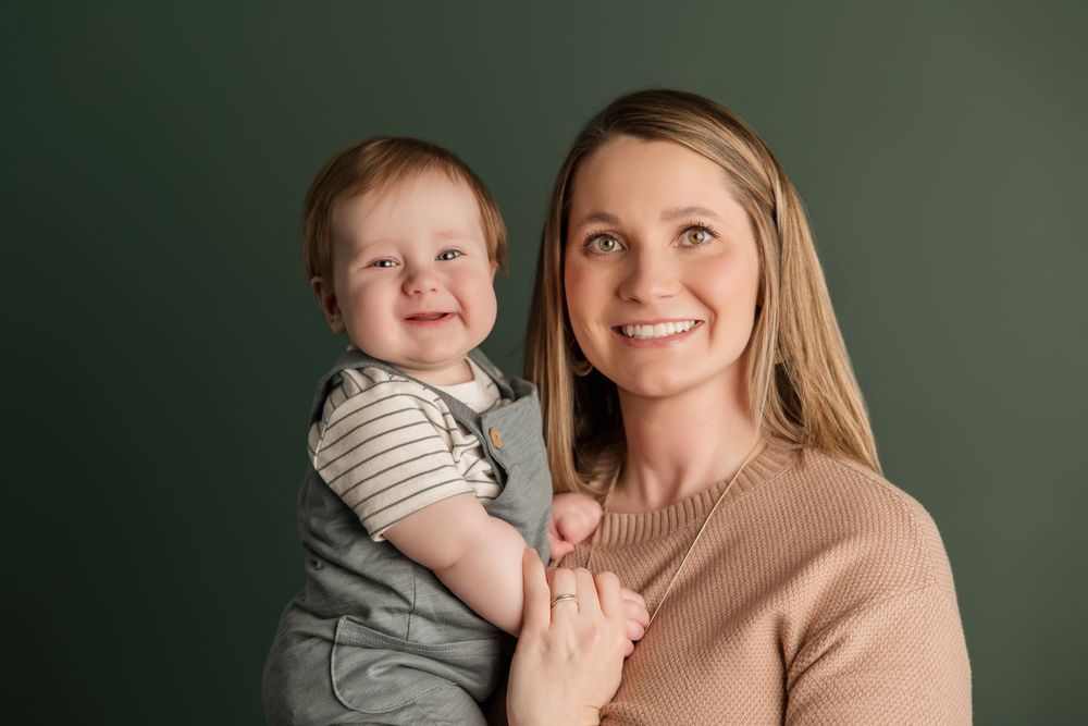 A parent and child share joyful moments together against a dark green studio backdrop.