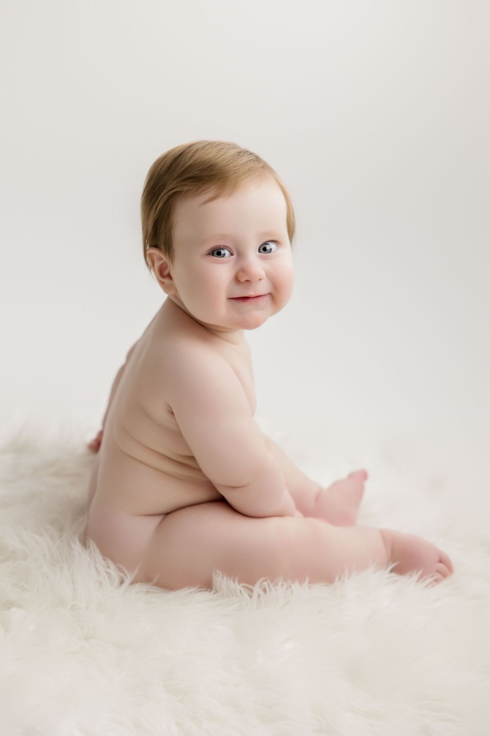 Chubby baby smiling and sitting on soft white fur in series of heartwarming portraits showing different poses.