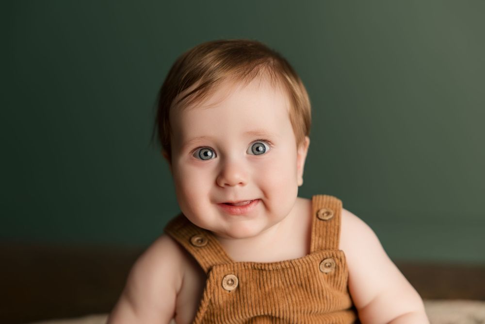 Child wearing brown overalls sits beside vintage wooden Coke crates against a green wall.