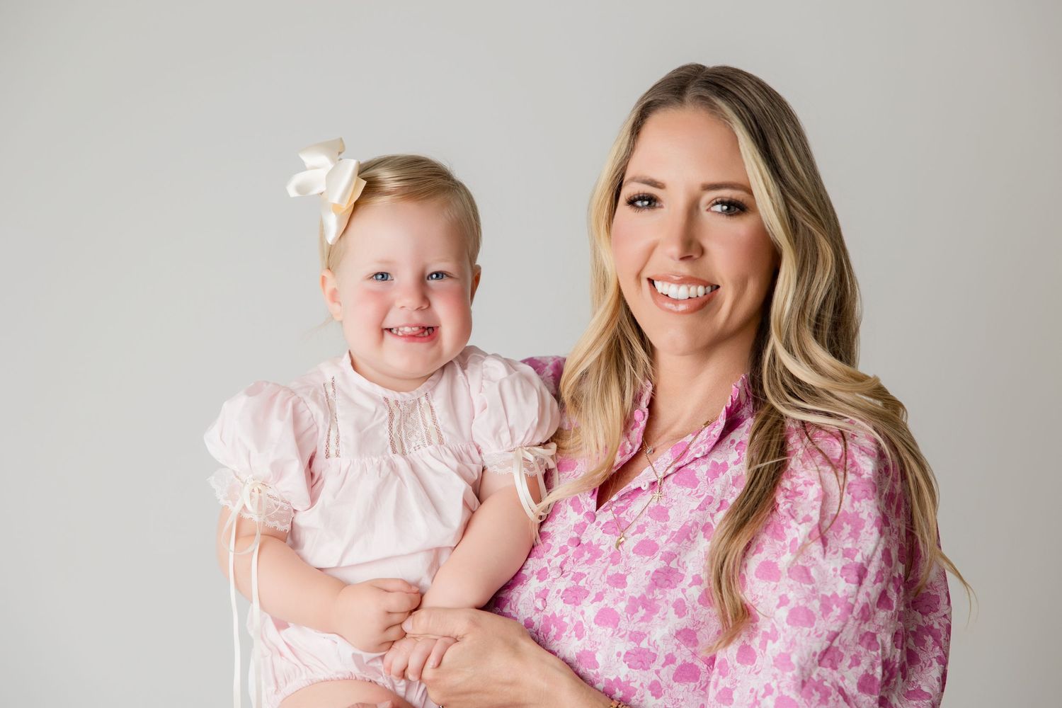 A family in coordinating pink outfits poses together for a cheerful portrait session against a light backdrop.
