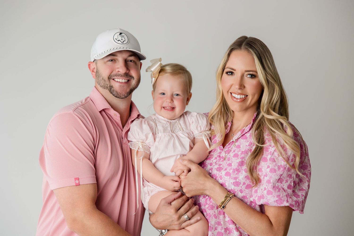 A family wearing coordinated pink and white outfits poses together in a series of professional portraits.