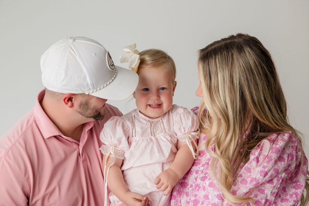 A family in pink clothing embracing and sharing playful moments during a portrait session.