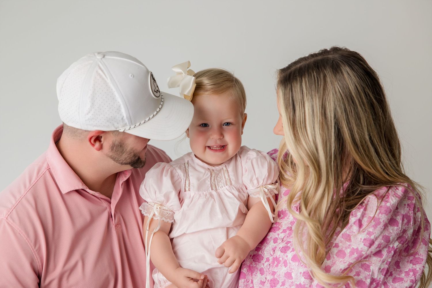 A family in pink clothing embracing and sharing playful moments during a portrait session.