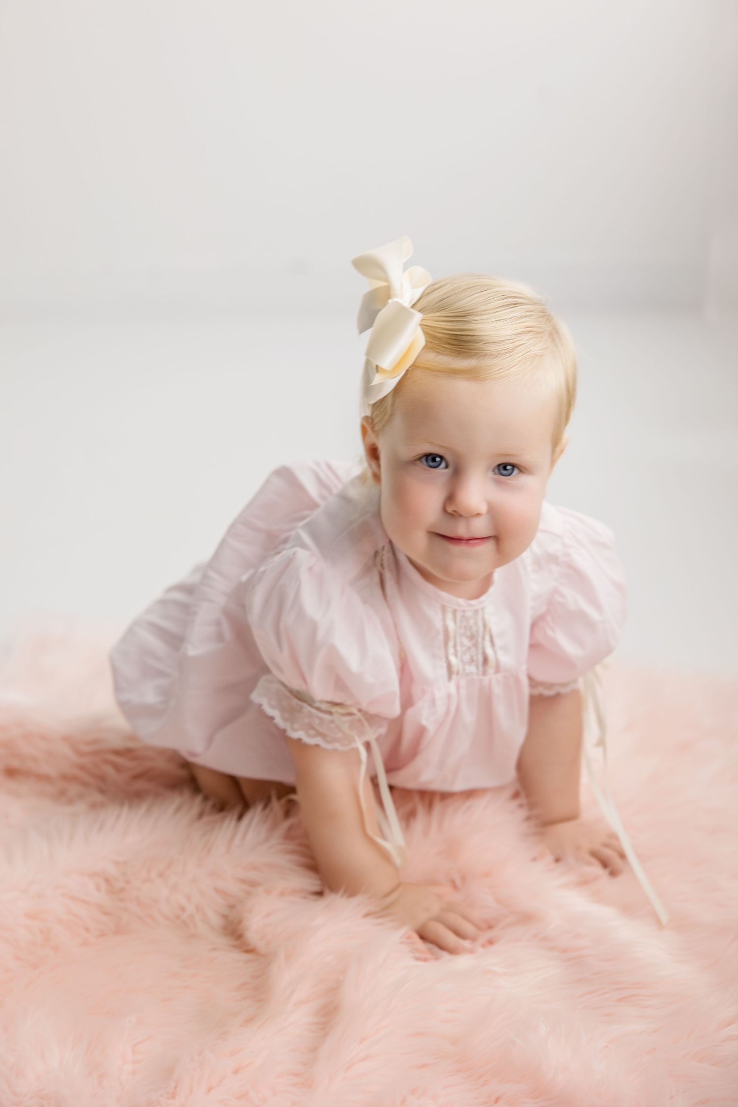 Sweet baby in pink dress crawls and plays on soft blush pink blanket or rug in three charming studio portraits.