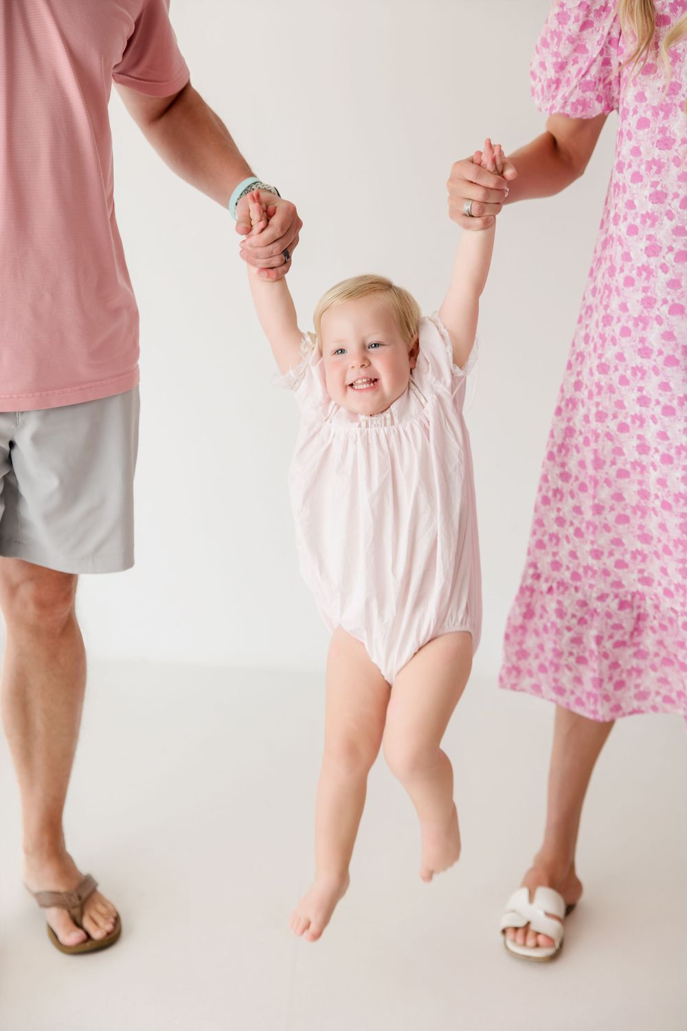 Family members in coordinating pink outfits show their feet while standing against a white background.