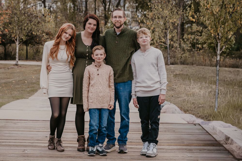 Family of five smiling together on a wooden boardwalk surrounded by autumn foliage.