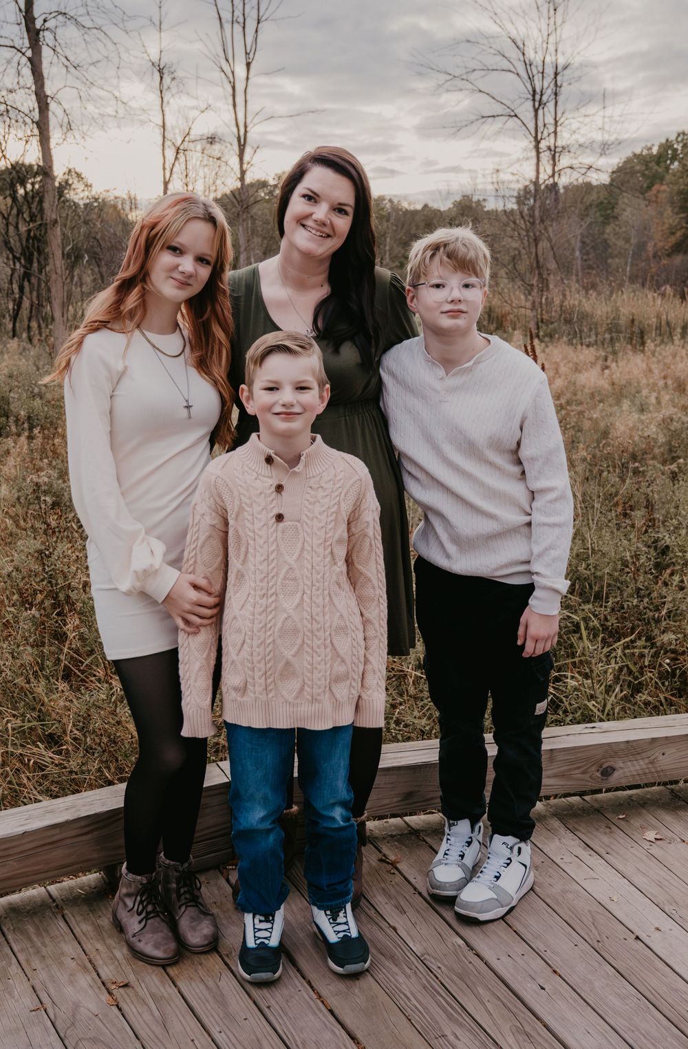 Mother smiling with her three children on a wooden deck surrounded by fall trees and brush.
