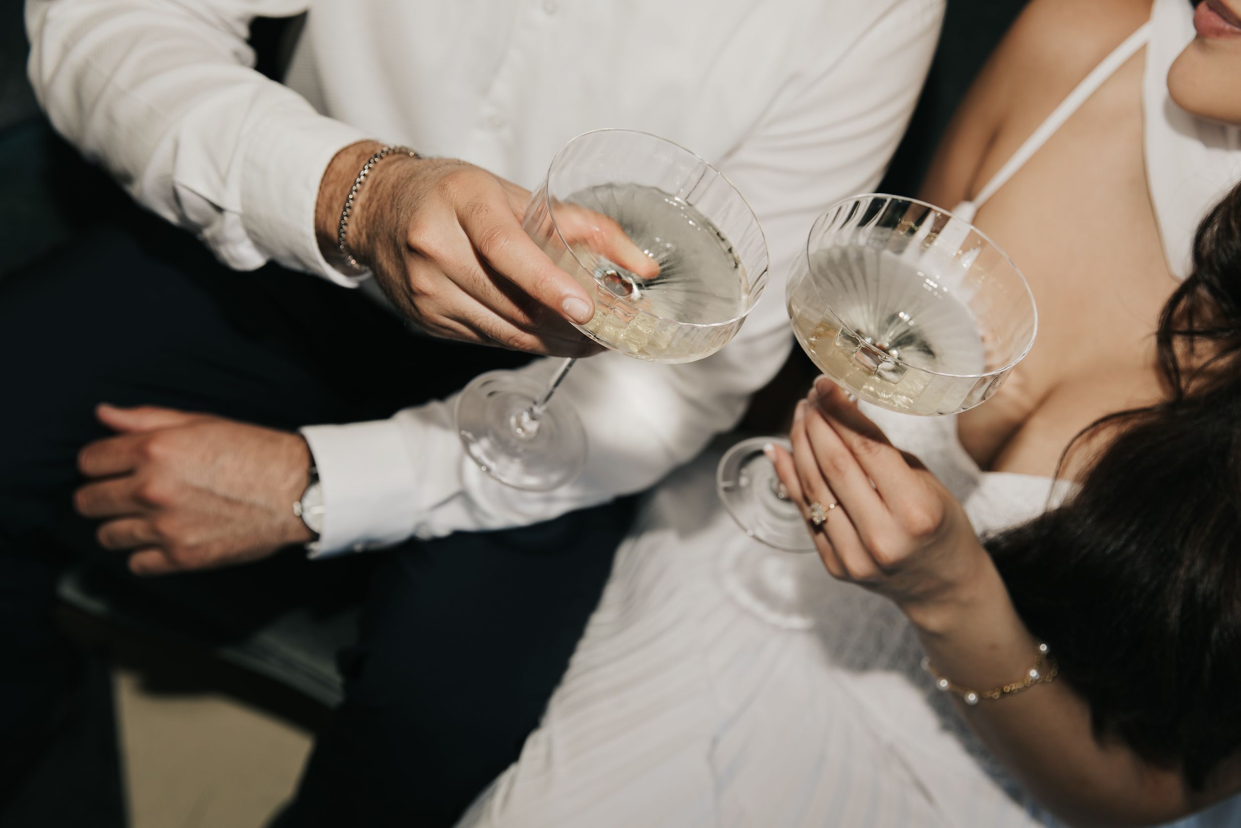 Two people in formal attire toast with coupe champagne glasses during a celebration.