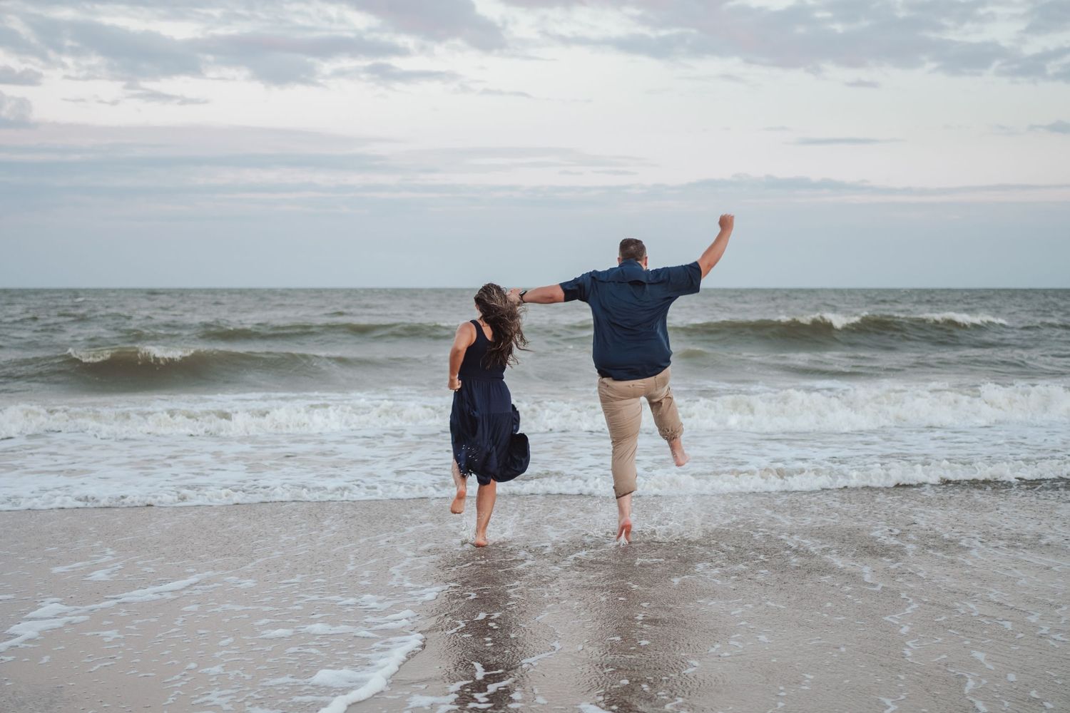 People enjoy splashing and playing in the shallow ocean waves at the beach on an overcast day.