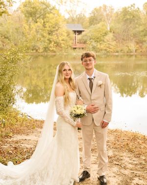 A wedding photoshoot by a lake with fall foliage and natural lighting.