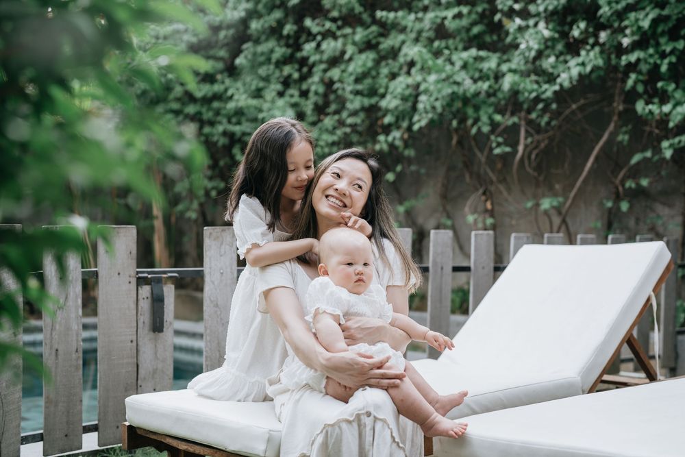 Family wearing white outfits relaxing together on outdoor patio furniture in a garden setting.