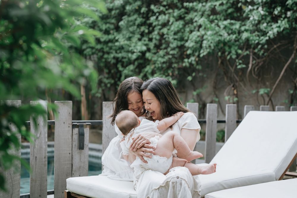Candid family moment captured outdoors with white cushioned seating and green foliage background.