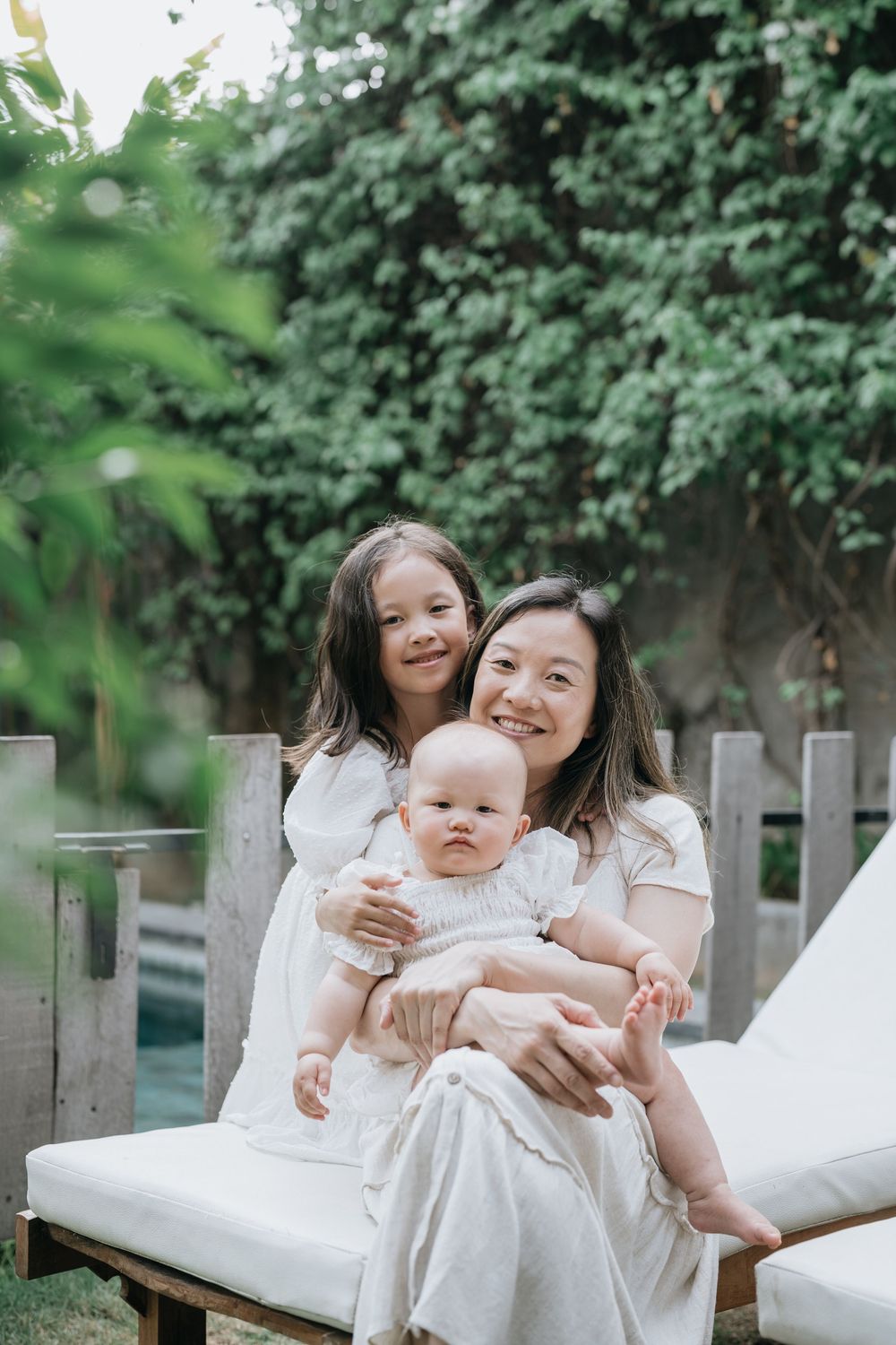Joyful outdoor family photoshoot with everyone dressed in white against lush greenery.