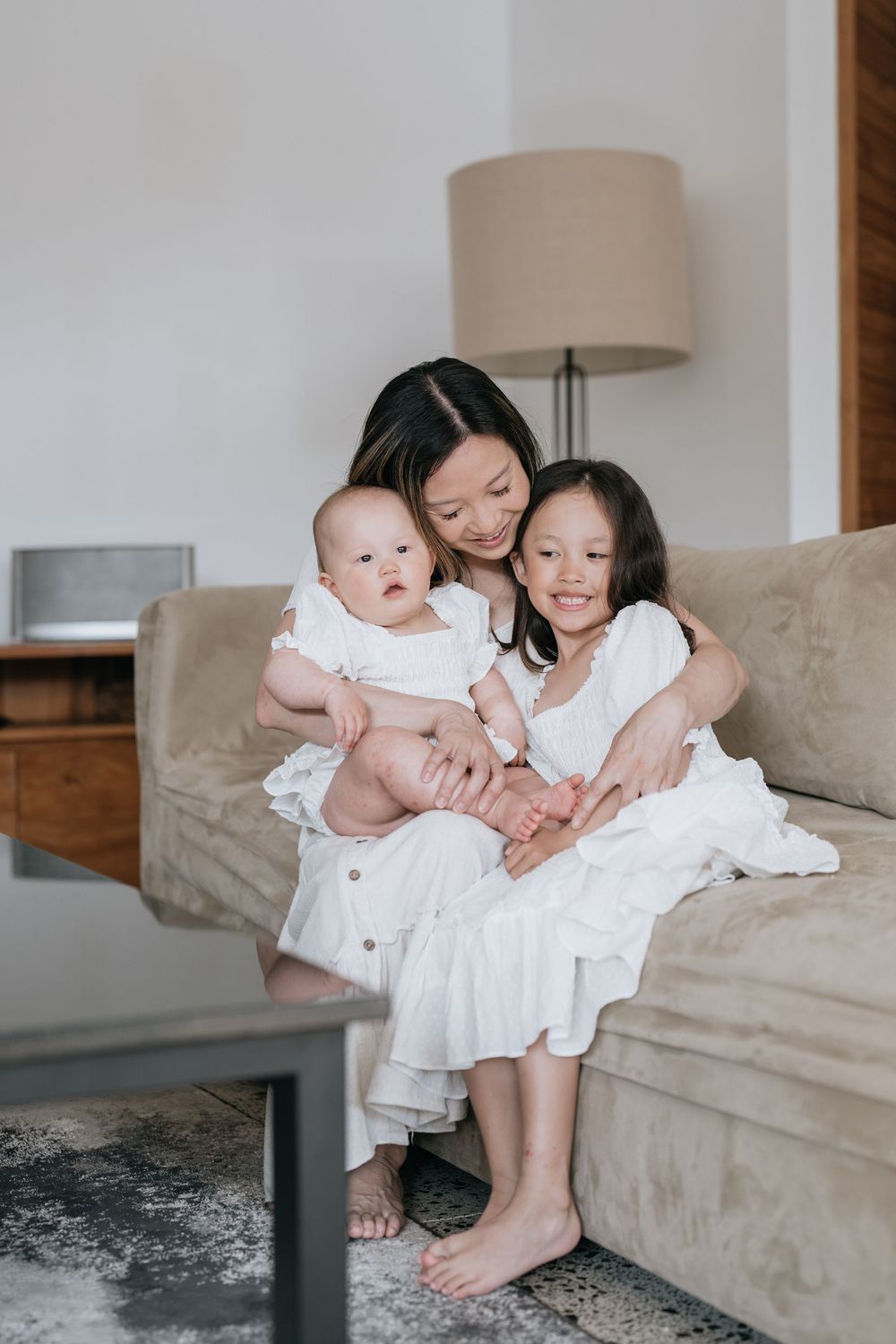 Family members share tender moments on a beige couch in a bright living room.