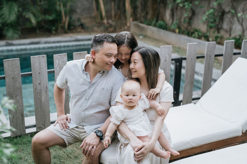 Casual family portrait session on wooden outdoor furniture with white cushions.