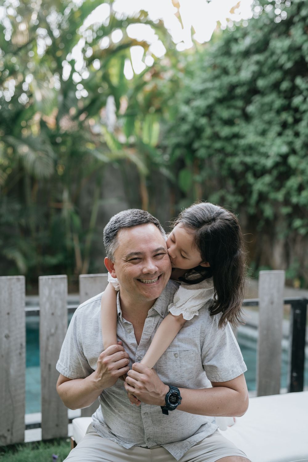 Intimate family moments captured on outdoor patio furniture against green garden backdrop.