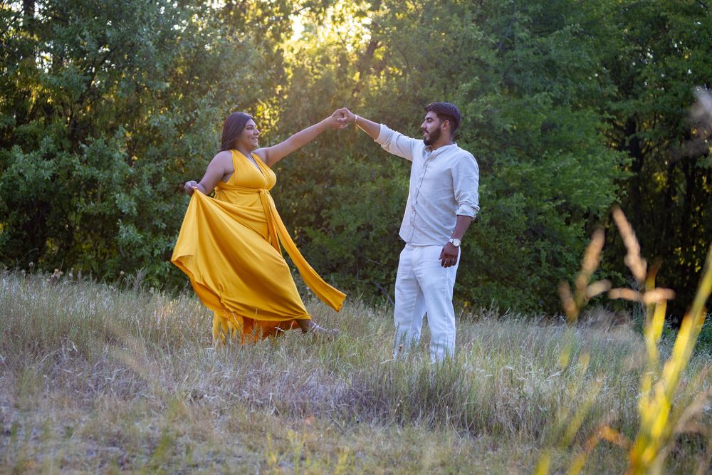 A couple in white and yellow clothing dance playfully together in a sunlit meadow during golden hour.