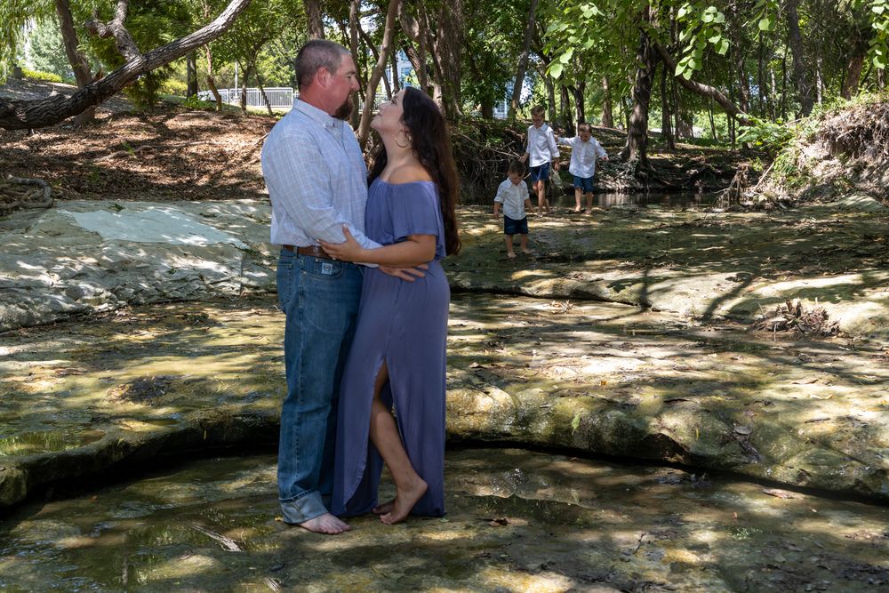 Couple sitting on rocks by a stream in a shady forest setting enjoy a peaceful outdoor moment together.