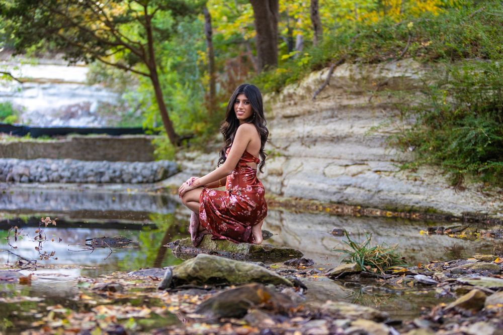 Scenic outdoor photoshoot at a cascading waterfall with stone steps surrounded by lush greenery and autumn foliage.