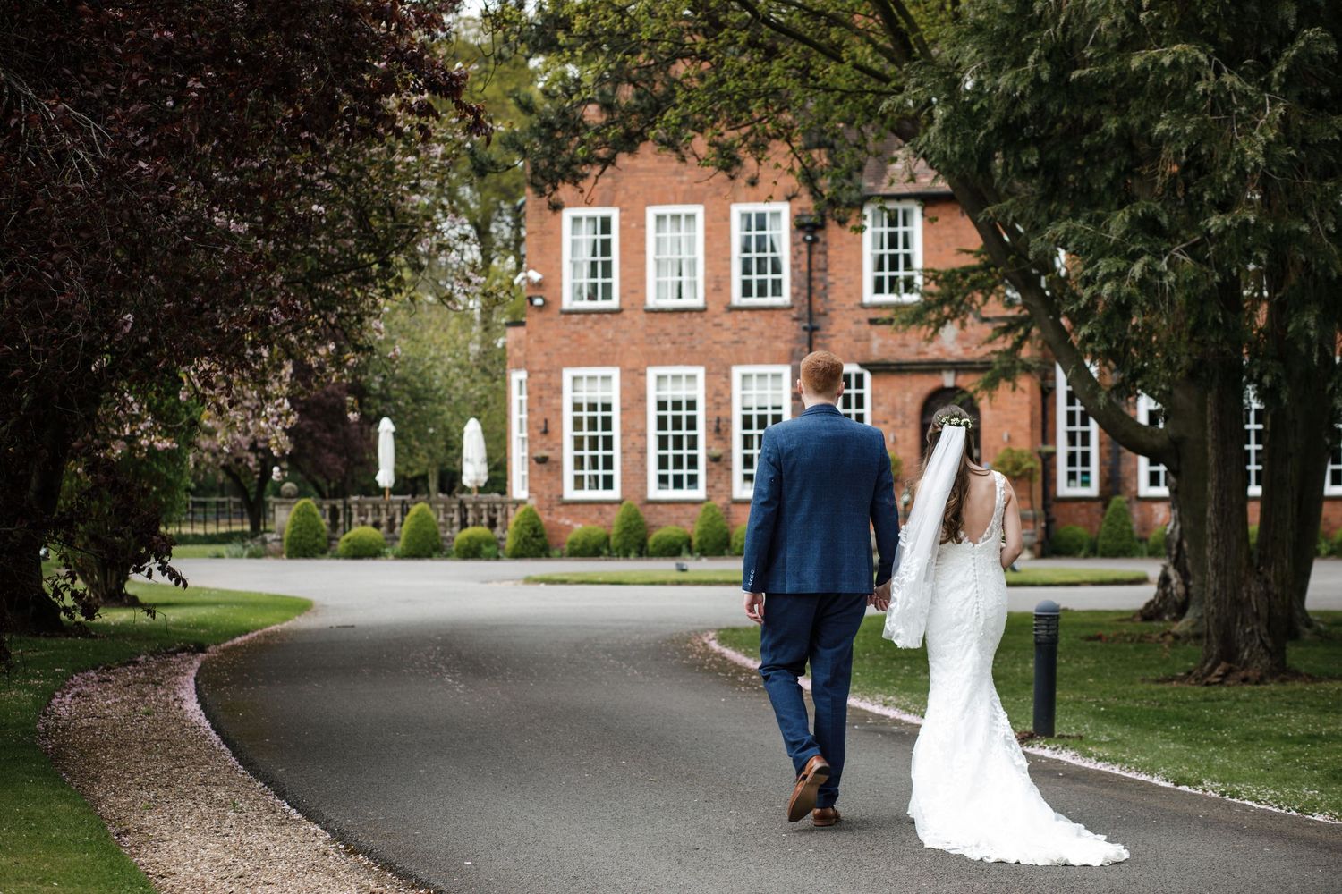 Bride and groom walking along the tree-lined Kelham House driveway towards the house