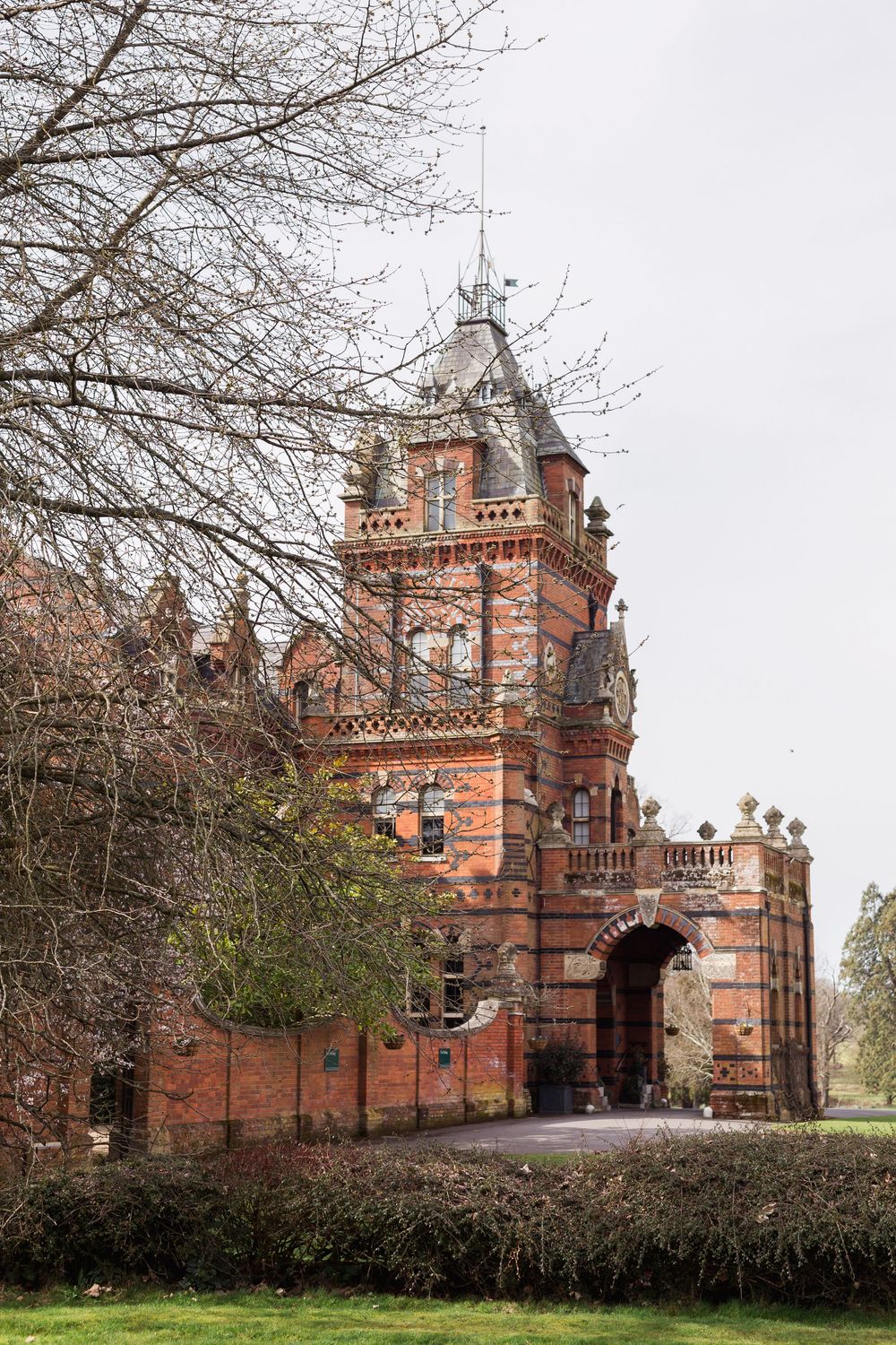 Historic red brick Victorian gatehouse with Gothic architectural details and arched entrance seen from multiple angles.