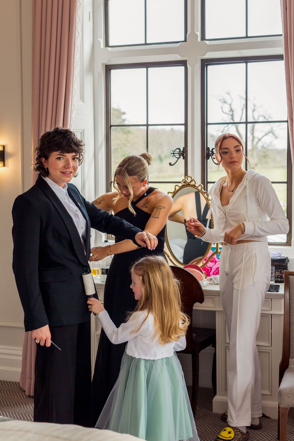 Wedding party members prepare for celebration in bright room with large windows.