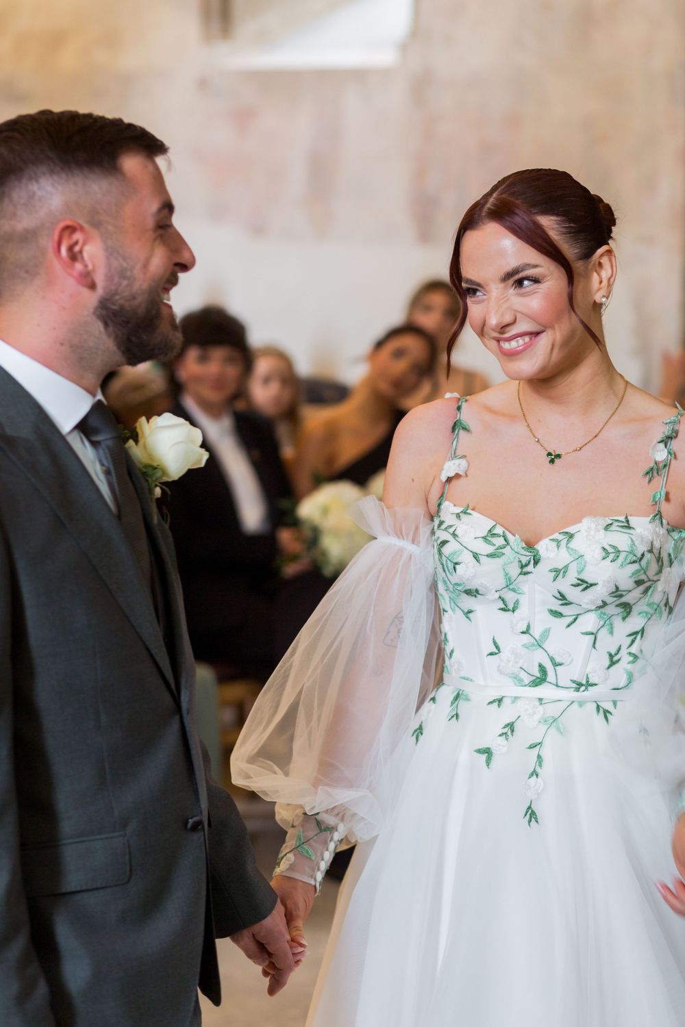A couple shares a loving moment at their wedding ceremony, with the bride wearing a unique floral-embellished white gown.