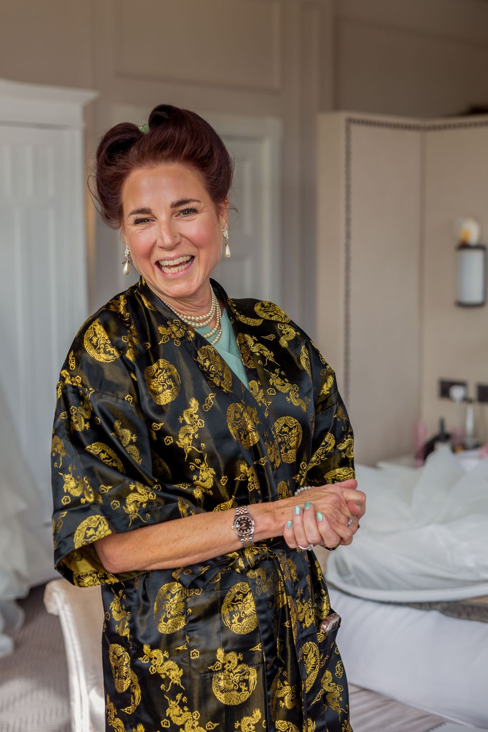 A person in a black and gold patterned robe smiles while sitting on a bed.
