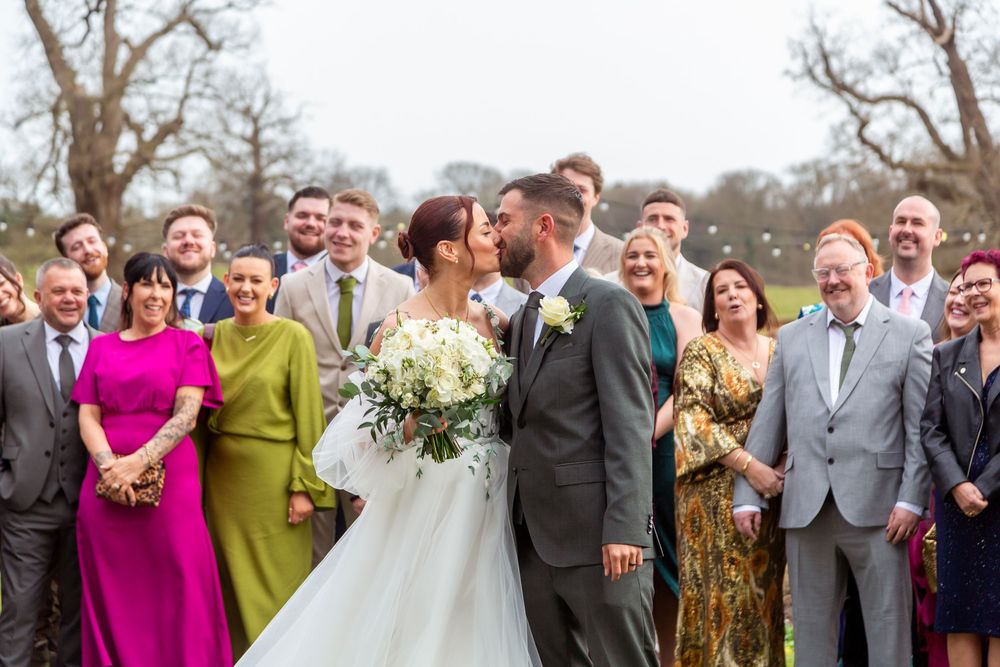Wedding party gathers outdoors in winter with guests wearing colorful attire while couple shares intimate moment.
