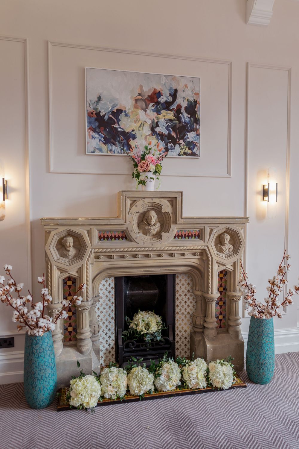 Elegant fireplace mantel decorated with turquoise mason jars and white hydrangea flowers in a classic white paneled room.