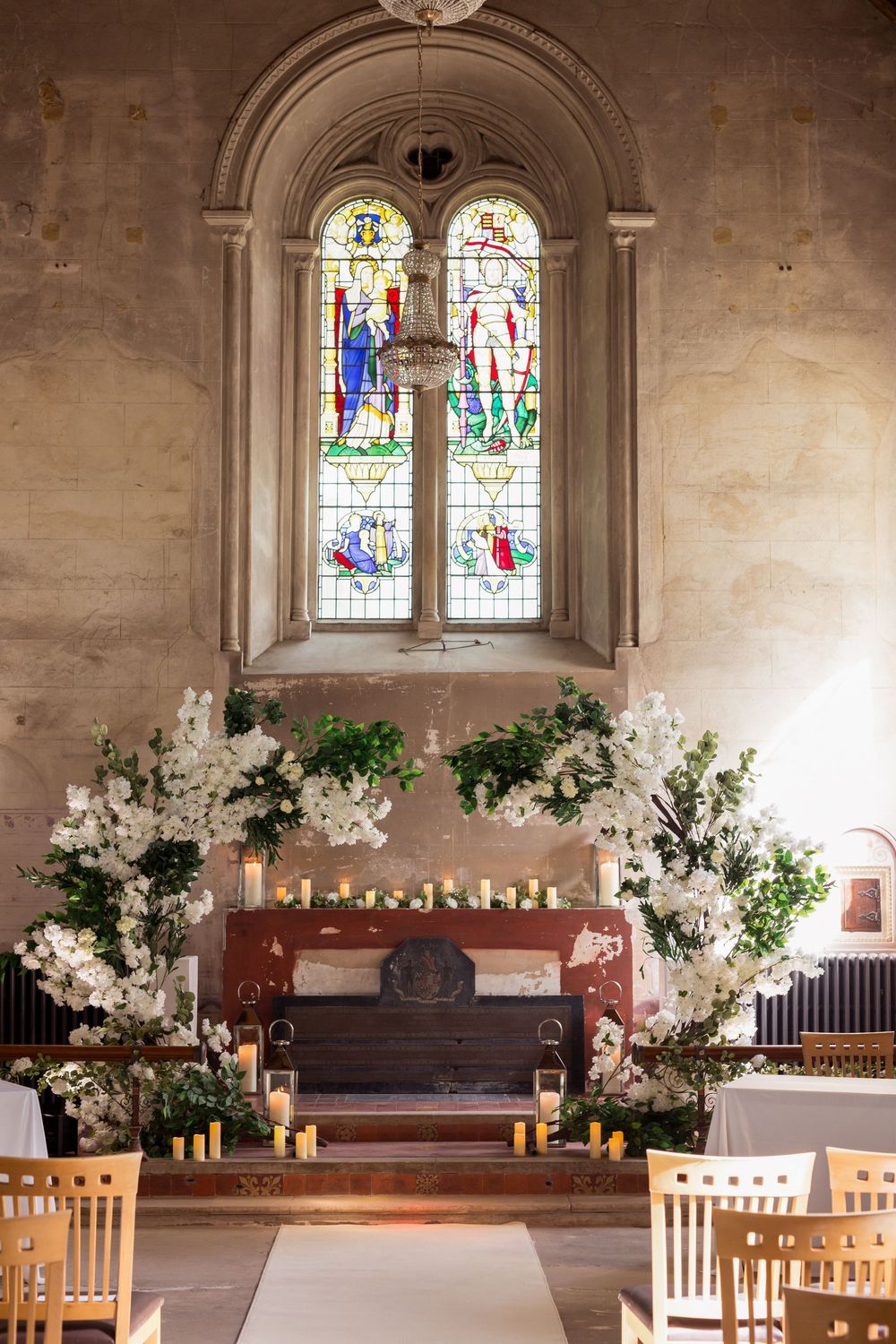 Church interior decorated with floral arrangements and candles for a wedding ceremony, featuring stained glass windows and wooden pews.