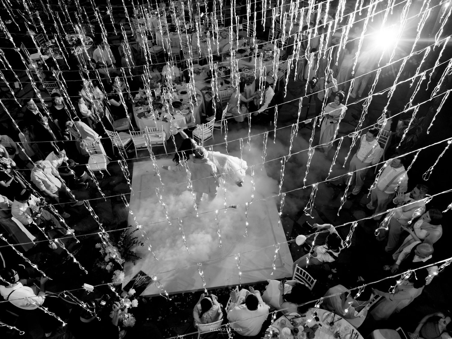 Black and white aerial view of wedding first dance surrounded by cascading string lights and guests.