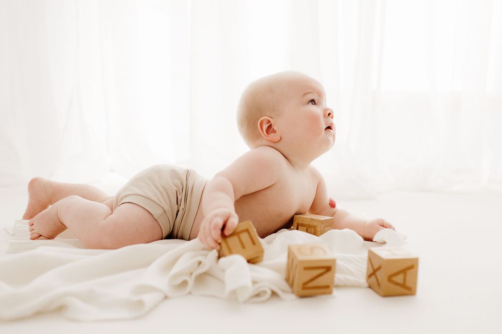 Baby lying on white blanket with wooden alphabet blocks.