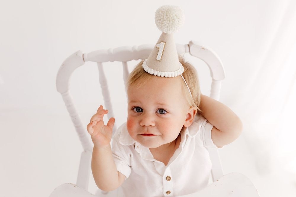 Baby wearing crown and white outfit during first birthday cake smash session.