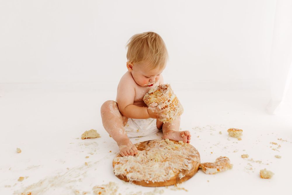 Baby playing with smashed cake on white floor during birthday photoshoot.
