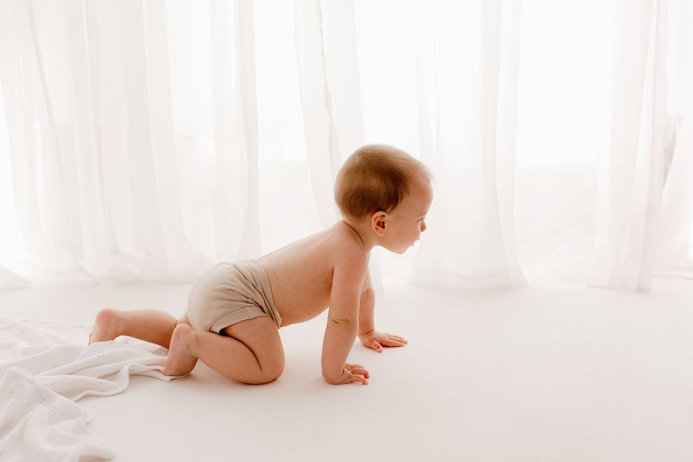 Baby crawling on white floor during bright studio photography session.