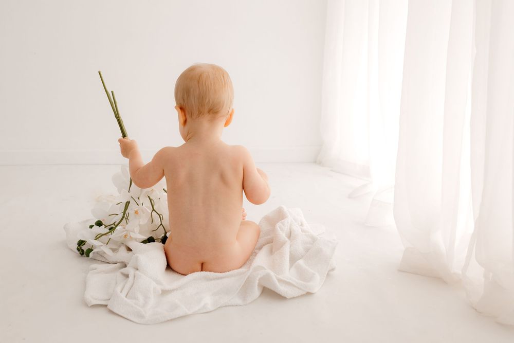 Baby sitting on white floor with decorative elements during photoshoot.