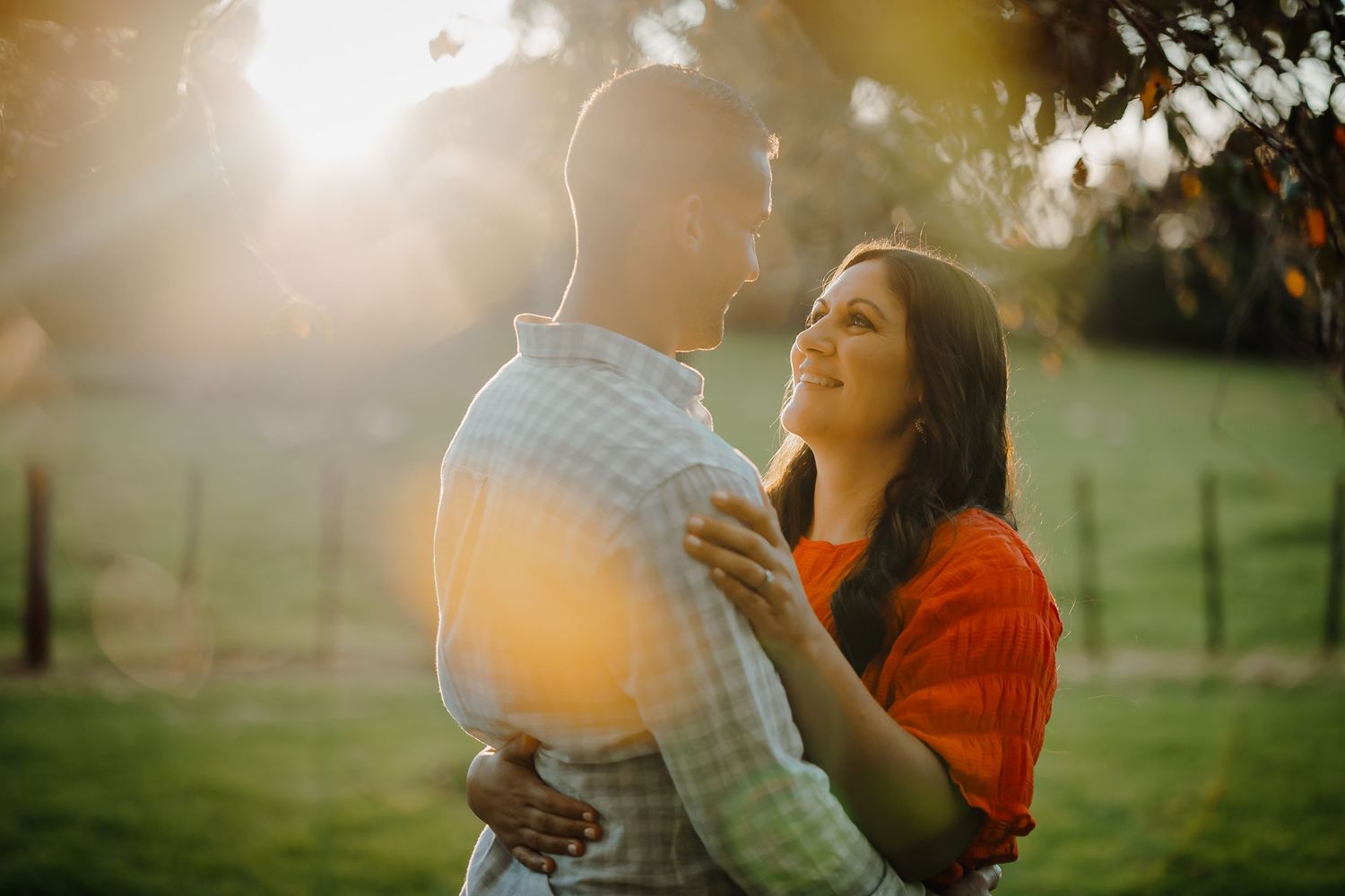 A couple embraces in a sunny park during golden hour as sunlight creates a warm glow around them.