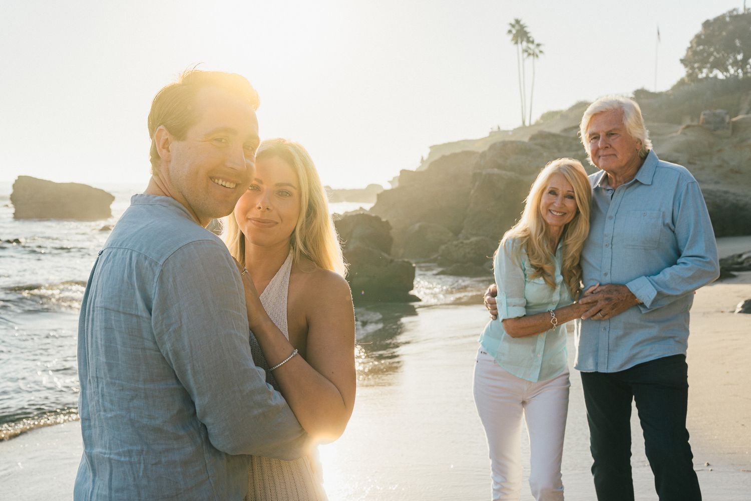 Newlyweds embracing on a beach while mom and dad also embrace themselves full of pride - Mariano Alvarez family photography Newport Beach