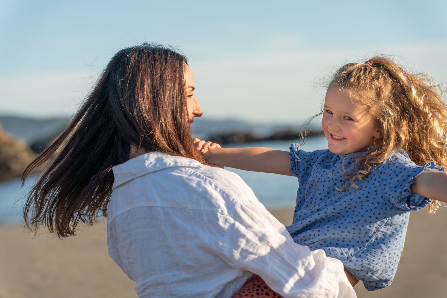 A tender moment between parent and child playing together on a sunny beach against a blue sky.