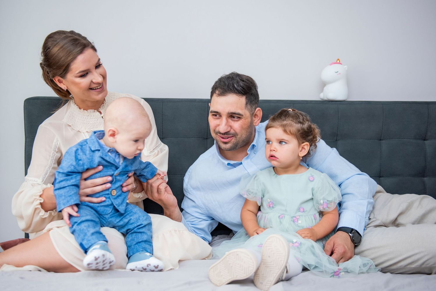 Family relaxing together on gray couch with infant in blue outfit.