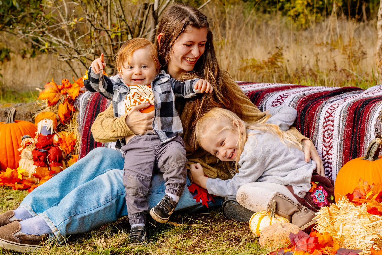 Young woman with two toddlers enjoying a fall outdoor photo session surrounded by pumpkins and autumn leaves.