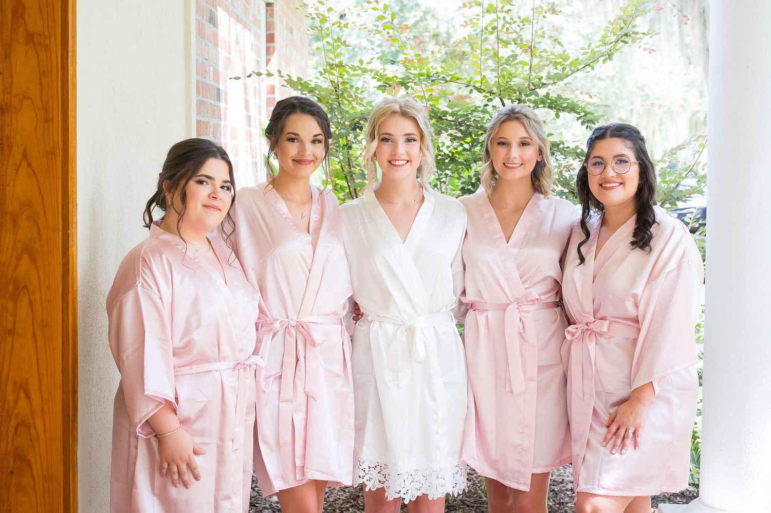 Bridesmaids in matching pink robes gather together during wedding preparations.