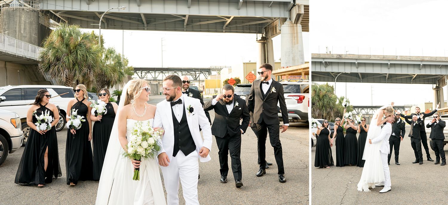 Wedding party in black and white attire walking together outdoors near urban bridge.