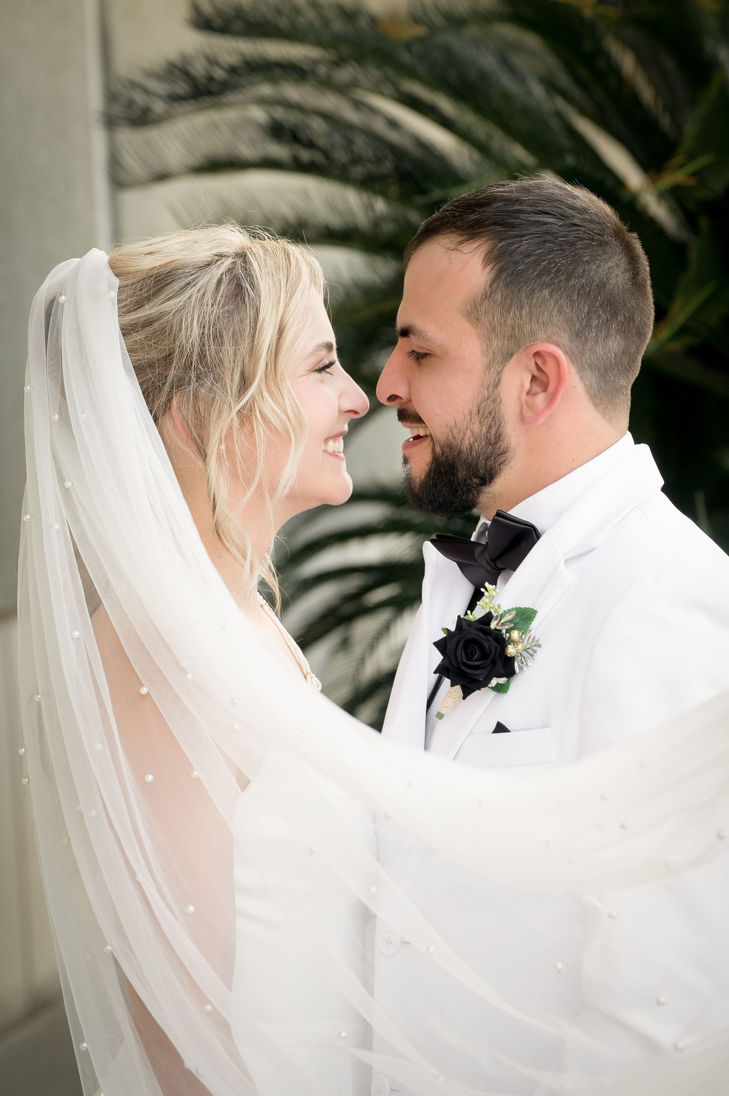 Intimate moment between newlyweds sharing laughter against palm tree backdrop.
