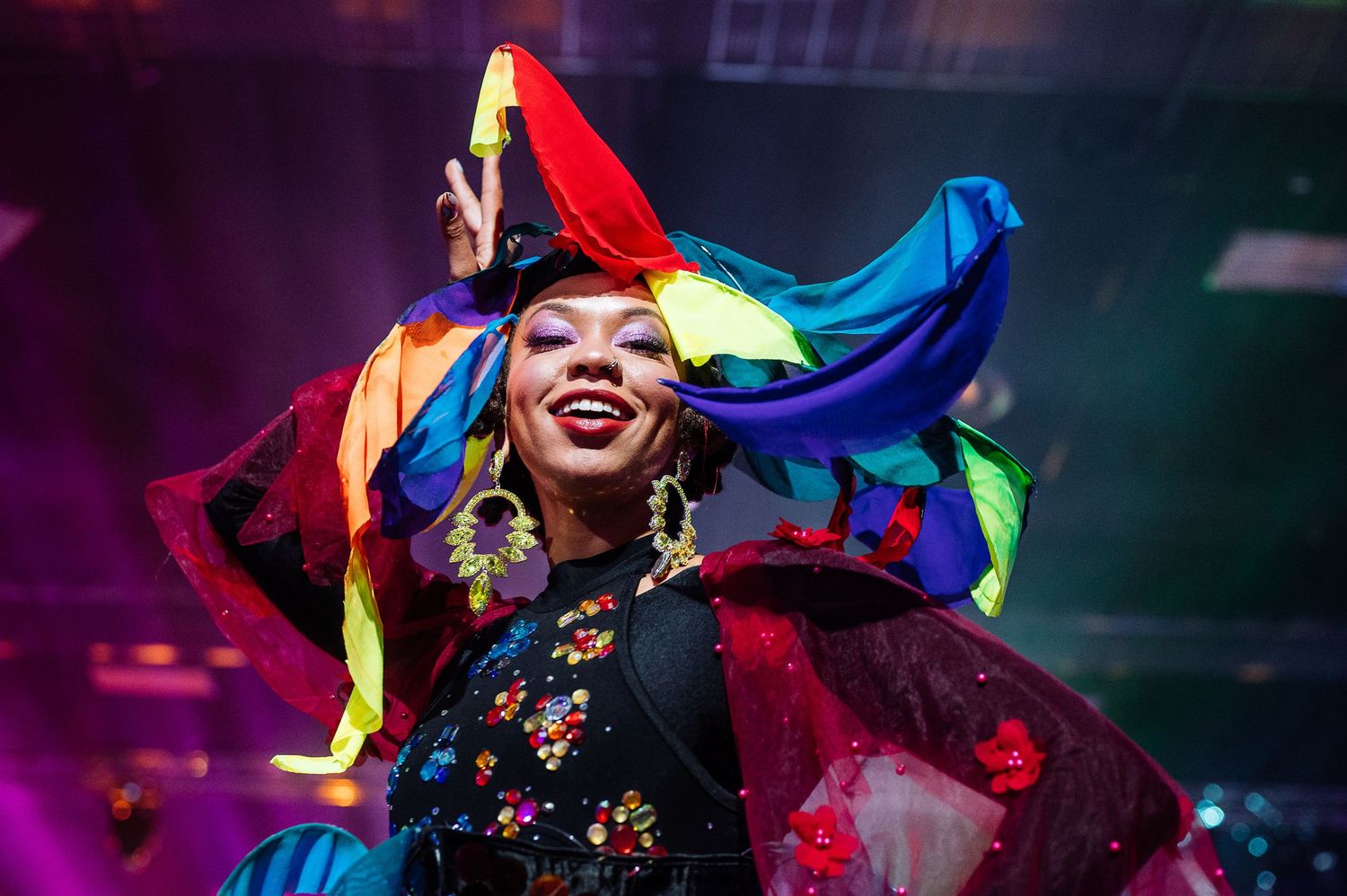 Colorful carnival performers in vibrant costumes under dramatic stage lighting.