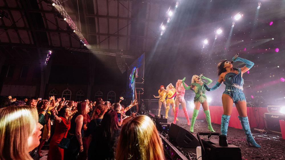 Concert venue panorama showing colorful stage lights and audience silhouettes.