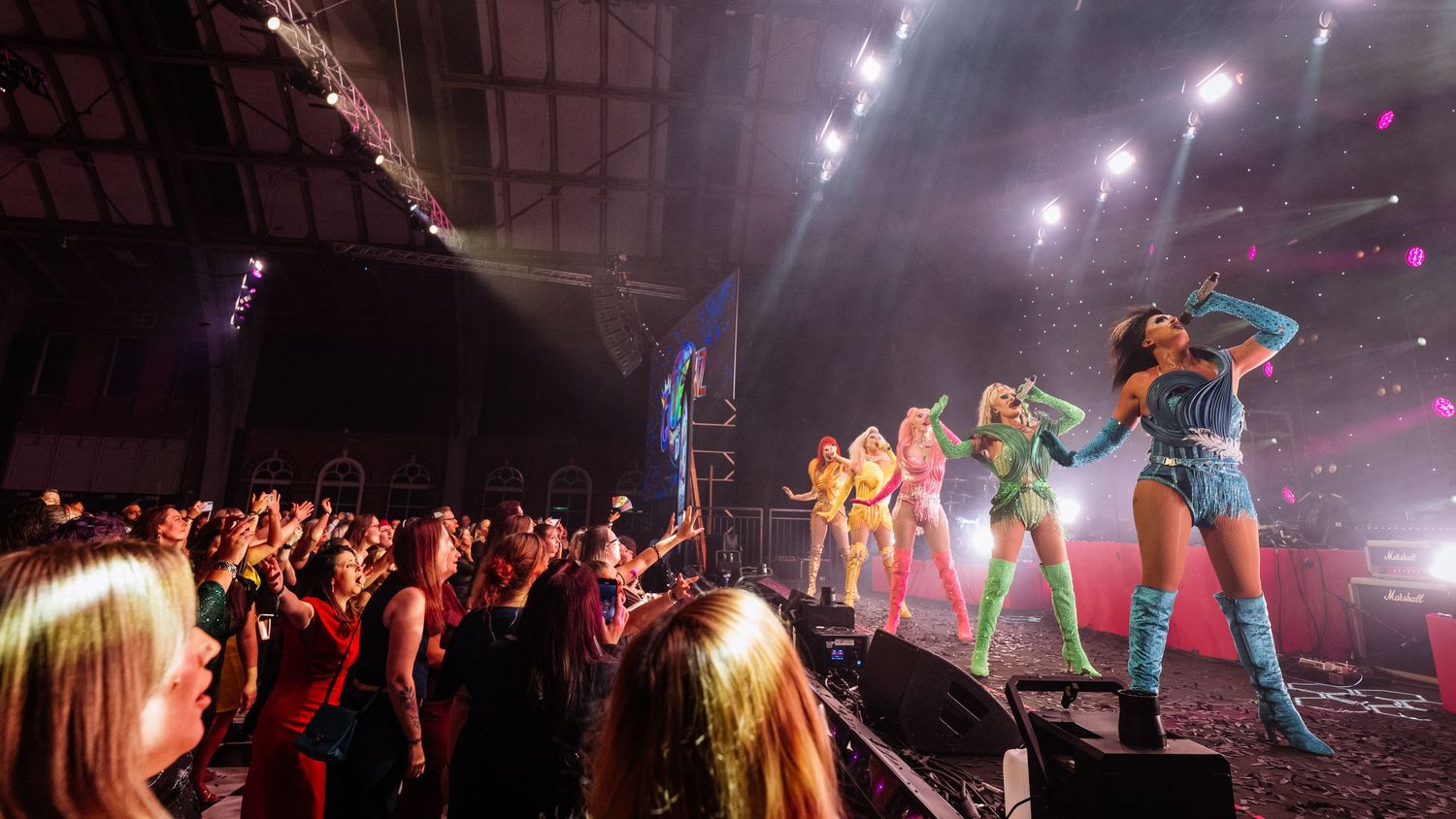 Concert venue panorama showing colorful stage lights and audience silhouettes.